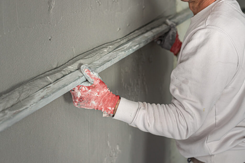 Machine plastering. Applying gypsum plaster by mechanized method on a wall. A worker hand removes excess plaster with leveler.